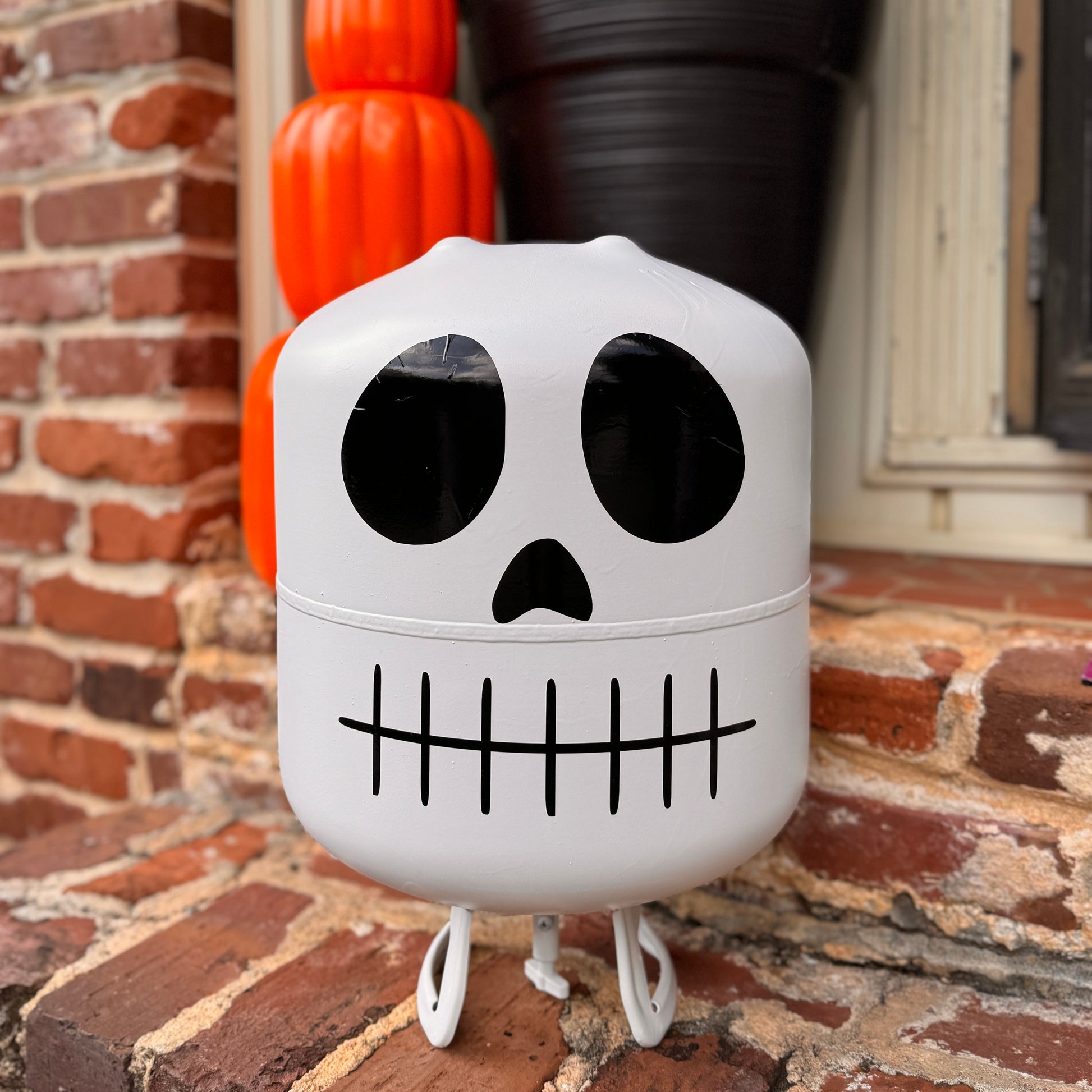 Halloween-themed skull-shaped container on a brick surface with pumpkins and flowers in the background.